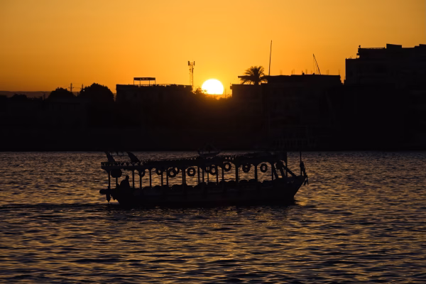 Ein Boot mit Dach und Reifen als Sto&szlig;f&auml;nger im Gegenlicht der Abendsonne auf dem Nil bei Luxor.