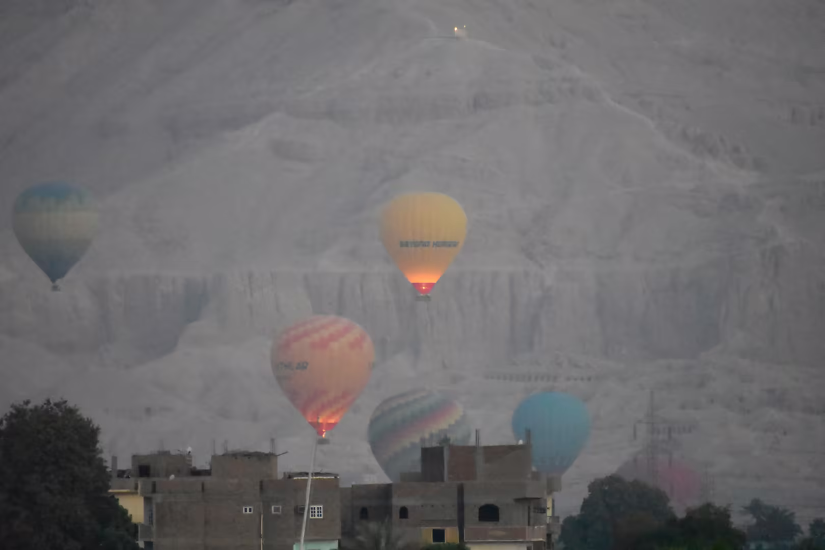 Mehrere Heißluftballons schweben im Morgenlicht über Wüste und Ruinen.