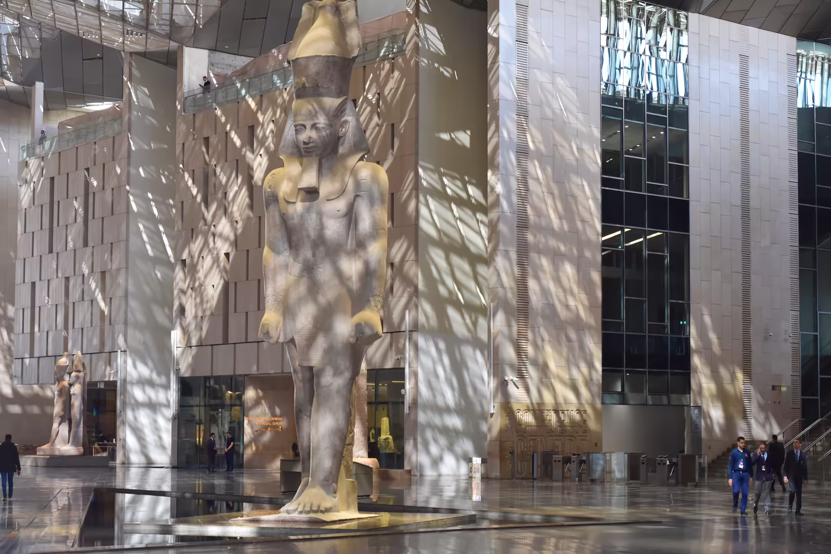 Eine hohe Statue aus hellem Stein steht in einer großen Halle, eine Besucherin gibt den Maßstab.