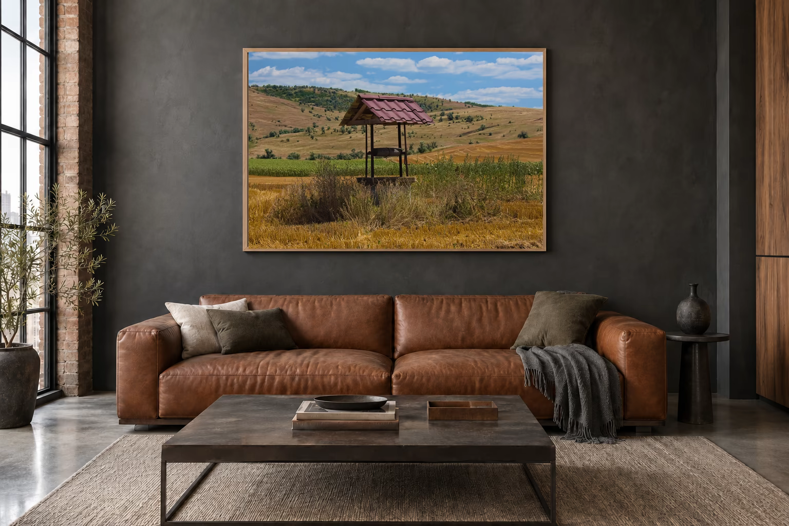 Das Werk an einer dunklen Wand im Loft über einem Ledersofa: Brunnen mit rotem Blechdach, 120 × 80 cm.