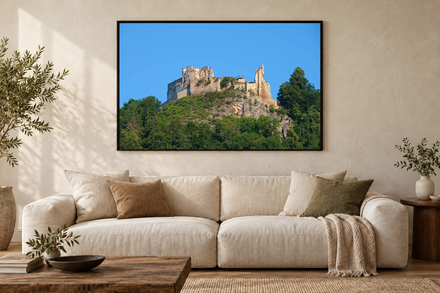 Das Werk an einer hellen Wohnzimmerwand über einem Sofa: Burgruine über dem Wald im Rahmen, 120 × 80 cm.