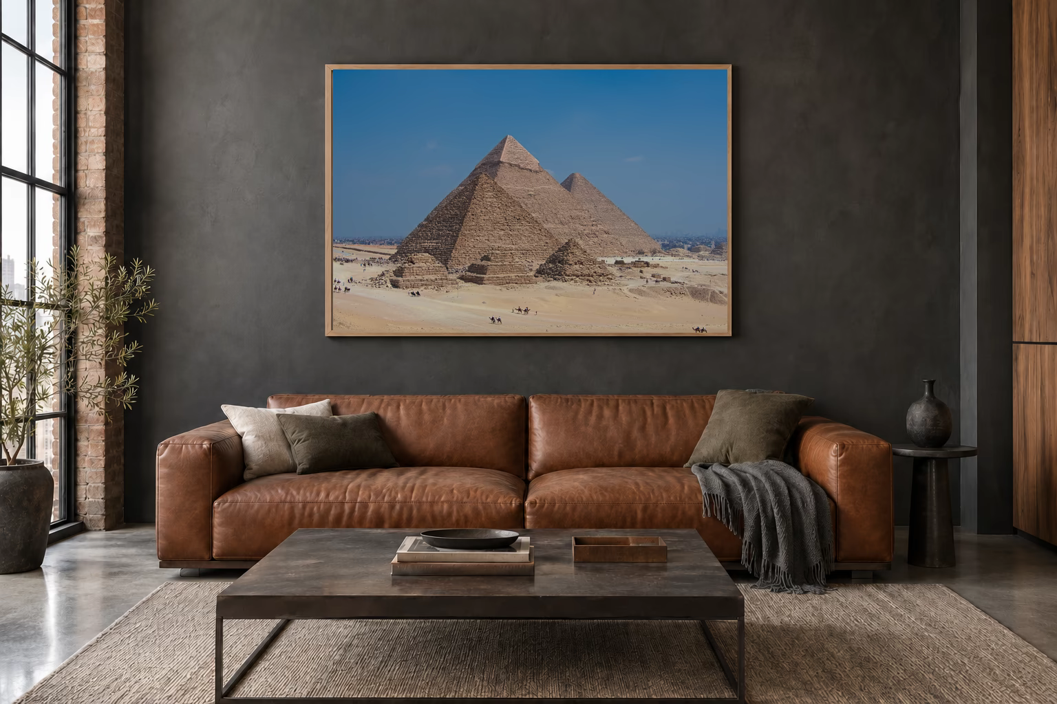 Das Werk an einer dunklen Wand im Loft über einem Ledersofa: Kamele vor den Pyramiden, 120 × 80 cm.
