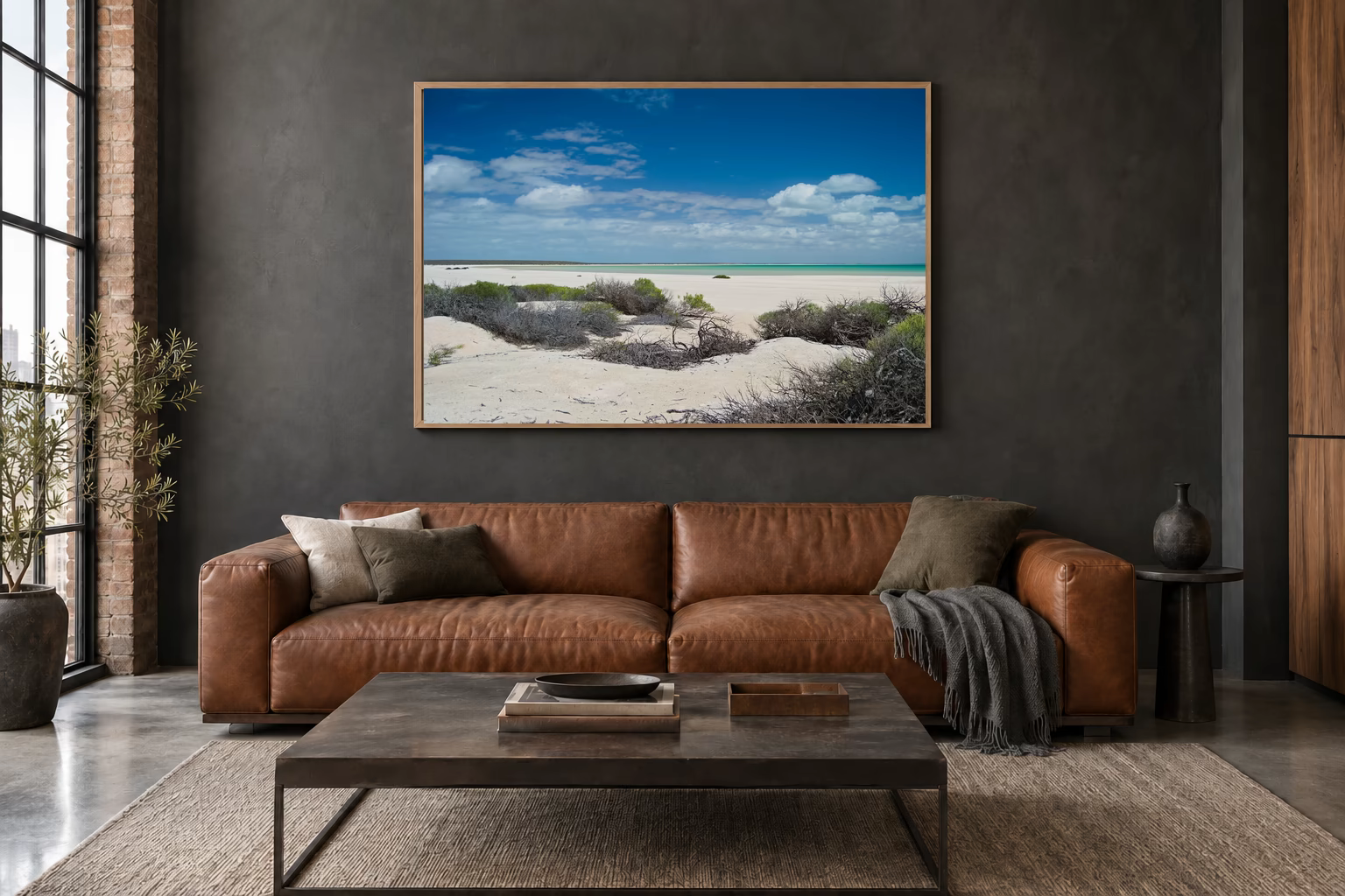 Das Werk an einer dunklen Wand im Loft über einem Ledersofa: Shell Beach, Helle Weite, 120 × 80 cm.